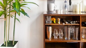 Una habitación con una planta grande en maceta, una cafetera y un estante con vasos y botellas.