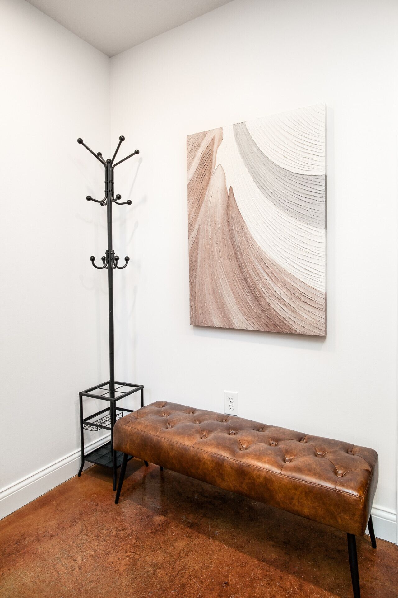 A room with a bench, a coat rack, and a wall-mounted artwork.
