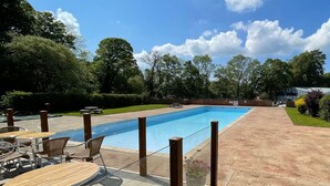 A rectangular swimming pool with a wooden deck and metal chairs. - Cozy Cottage Retreat on Glan Gwna Holiday Park (Caernarfon)