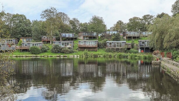 A lakeside residential area with multiple wooden houses, each featuring balconies and large windows. - Cozy Cottage Retreat on Glan Gwna Holiday Park (Caernarfon)