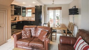 A compact living space with a kitchenette, a dining area, and a seating area with leather sofas. - Cozy Cottage Retreat on Glan Gwna Holiday Park (Caernarfon)