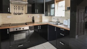 A modern kitchen with black cabinets, a stainless steel range hood, a built-in oven, a sink, and a window with blinds. - Cozy Cottage Retreat on Glan Gwna Holiday Park (Caernarfon)