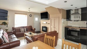 A compact living space with a sofa, a dining table, a TV, a fireplace, and a kitchen area with modern appliances. - Cozy Cottage Retreat on Glan Gwna Holiday Park (Caernarfon)