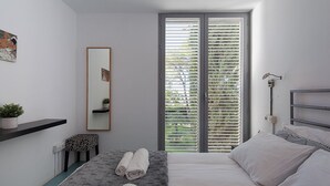 Une chambre à coucher moderne avec un lit, une table de chevet, un miroir et une fenêtre avec des stores.