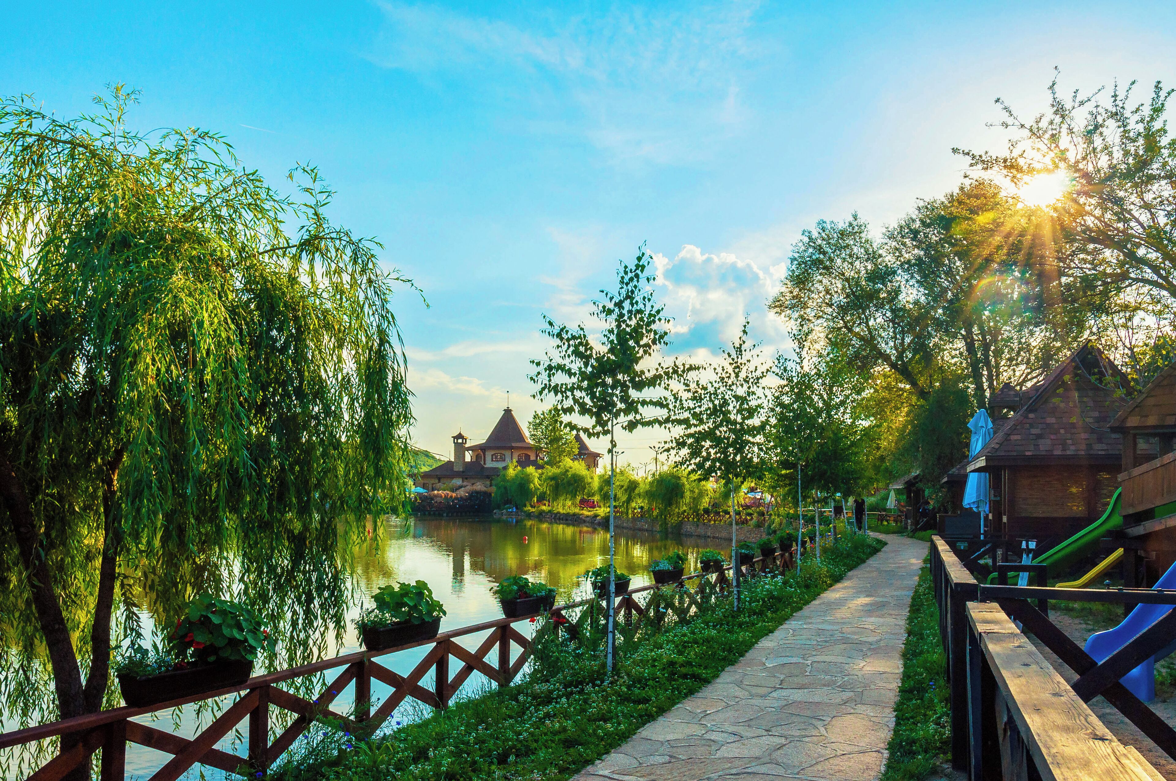 A riverside walkway with a wooden fence, a small building, and a playground with slides.