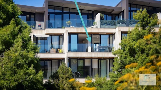 A multi-story modern building with large windows and balconies, surrounded by greenery.