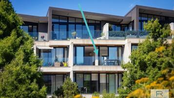 A multi-story modern building with large windows and balconies, surrounded by greenery.