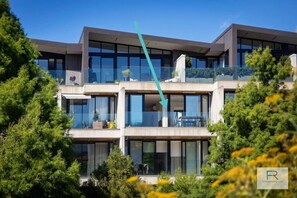 Un edificio moderno de varios pisos con amplias ventanas y balcones, rodeado de vegetación.