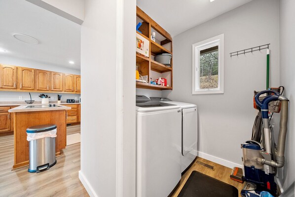 A compact kitchen with wooden cabinets, a built-in washing machine, and a vacuum cleaner.