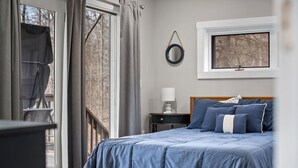 Une chambre à coucher avec un lit, une table de chevet, une fenêtre et une vue sur les arbres.