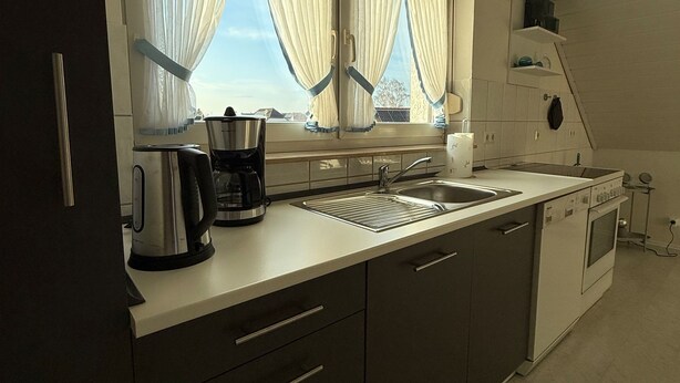 Una cocina moderna con ventana, cafetera, lavamanos y estufa.