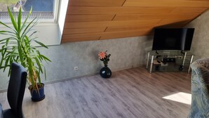 Una sala de estar moderna con techo de madera, un televisor de pantalla plana, una planta en maceta y un sofá.