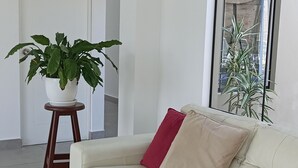 Een moderne woonkamer met een witte leren bank, een houten krukje met een plant in pot en een groot raam met uitzicht op het landschap.