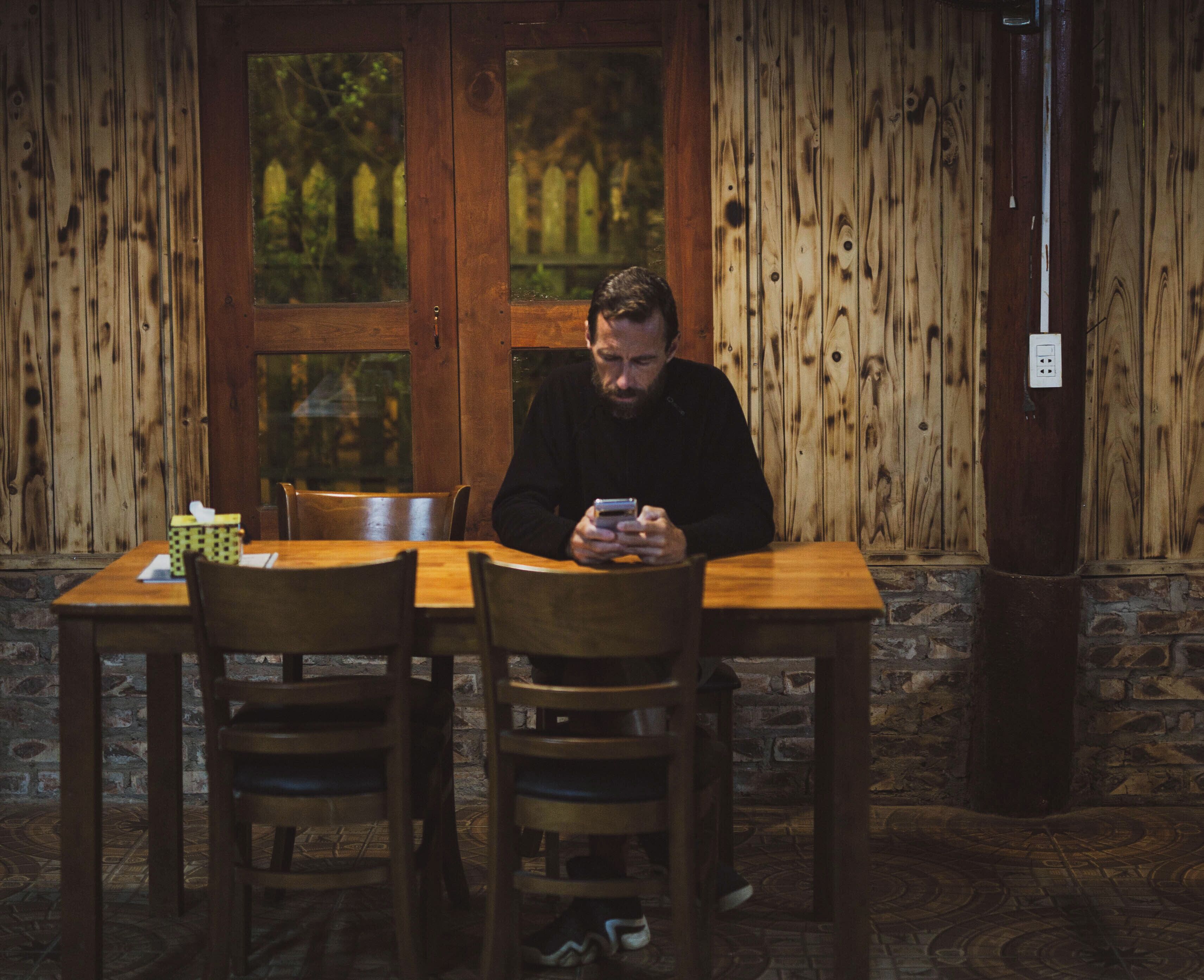 A man sitting at a wooden table in a room with wooden walls and a window.