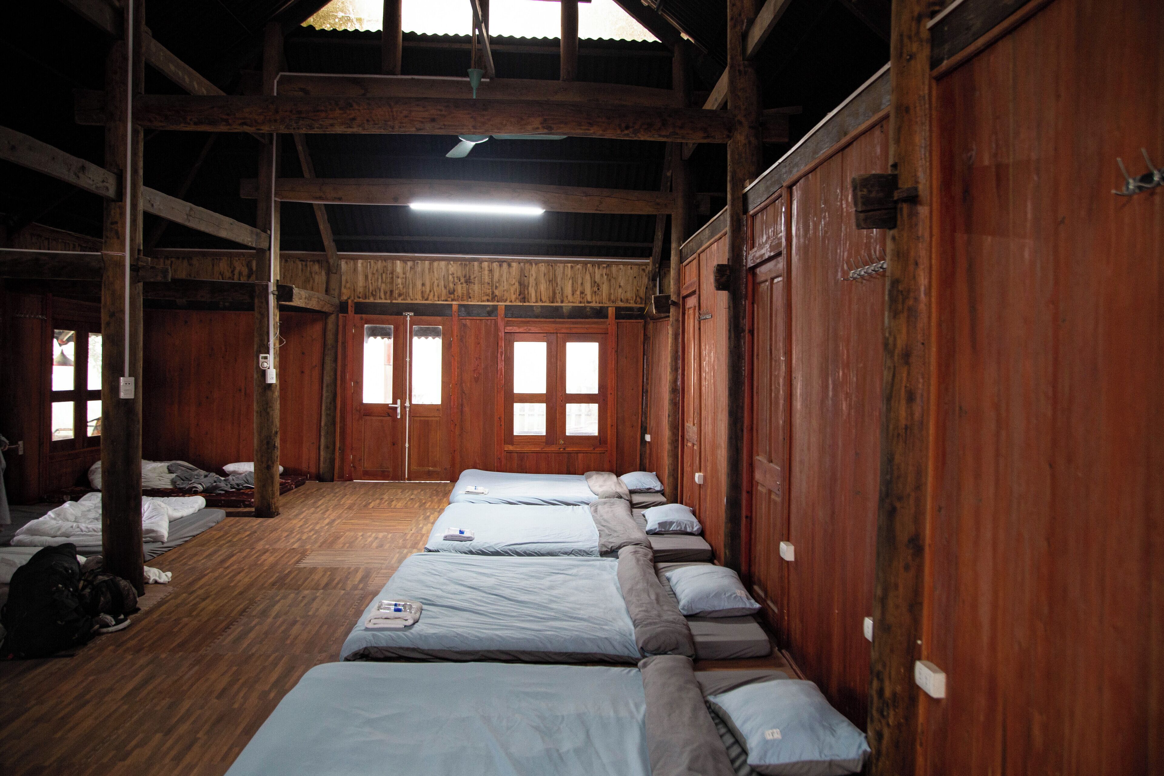 Una habitación con varias camas dispuestas en filas, paredes de madera y un techo alto con vigas a la vista.