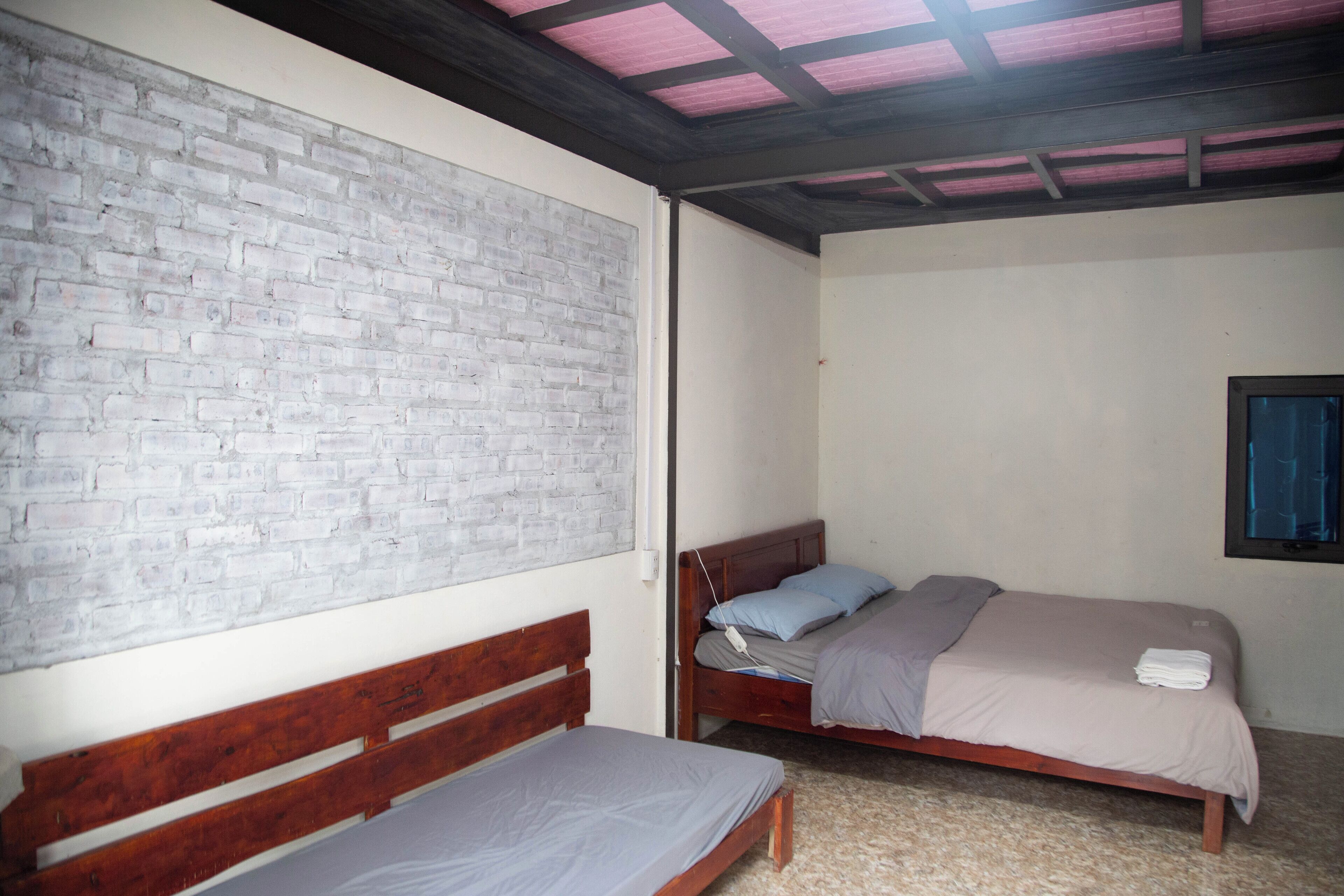 Una habitación con pared de ladrillo, dos camas de madera, una ventana y techo con vigas a la vista.