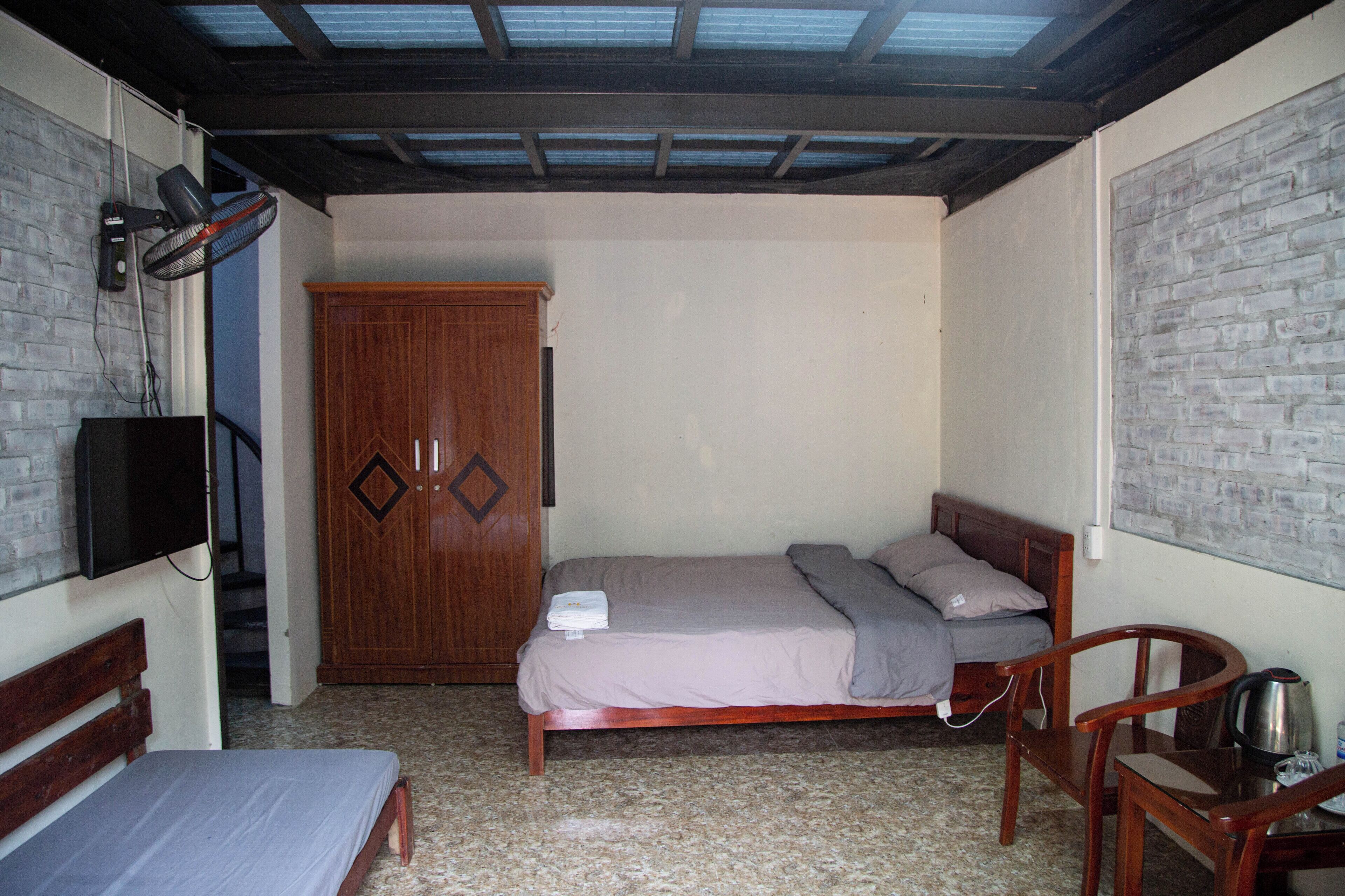 Un dormitorio con cama, armario de madera, escritorio con silla y televisor en la pared.