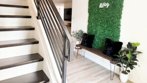 A staircase with dark wooden steps and a metal railing, leading to a room with a green wall and a bench with black cushions. - Pool House near Downtown Round Rock (Round Rock)