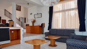 A modern living room with a sofa, two wooden side tables, a TV, a wooden reception desk, and a staircase. - Spacious & Private 6 bed villa close to Peyia - 5bed villa + 1bed granny annex (Peyia)