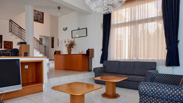 Una sala moderna con un sofá, dos mesitas de madera, un televisor, un mostrador de recepción de madera y una escalera.