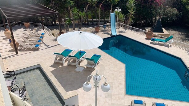 A swimming pool with lounge chairs and umbrellas, surrounded by trees and a pergola. - Spacious & Private 6 bed villa close to Peyia - 5bed villa + 1bed granny annex (Peyia)