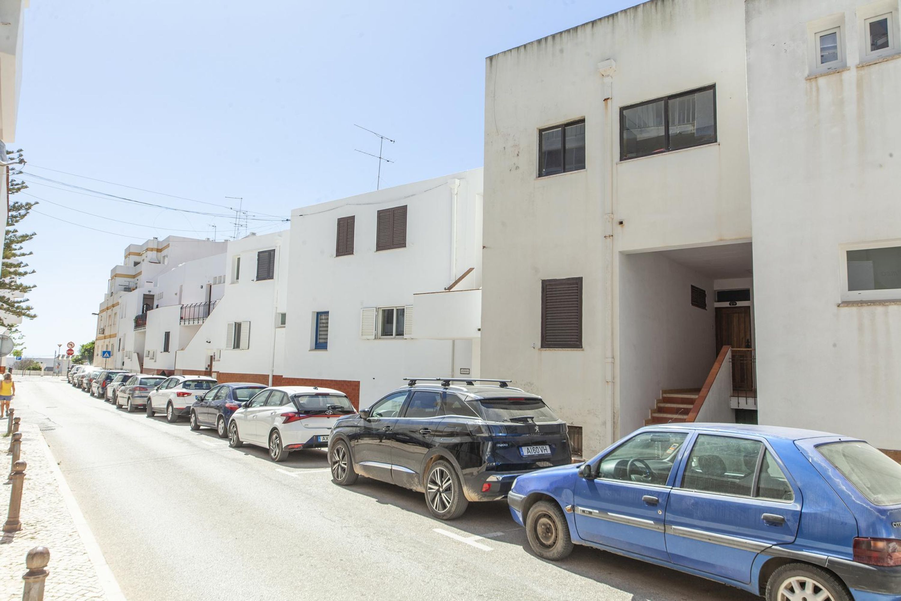 Une rangée de voitures garées le long d’une rue bordée d’immeubles blancs dotés de balcons et de fenêtres.