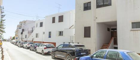 Une rangée de voitures garées le long d’une rue bordée d’immeubles blancs dotés de balcons et de fenêtres.
