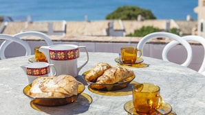 Ein Tisch gedeckt mit Croissants, einer Karaffe und Tassen, mit Blick auf die Küste.