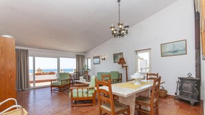 Ein geräumiges Wohnzimmer mit einem Holzessttisch, grünen Stühlen und Meerblick durch große Fenster.