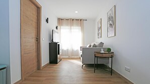 Een hal met een houten deur, een televisie, een bank en een kleine tafel met een plant.