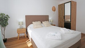 Een opgemaakt bed met kussens, een bedlamp, een klein tafeltje, een kamerplant en een spiegel.