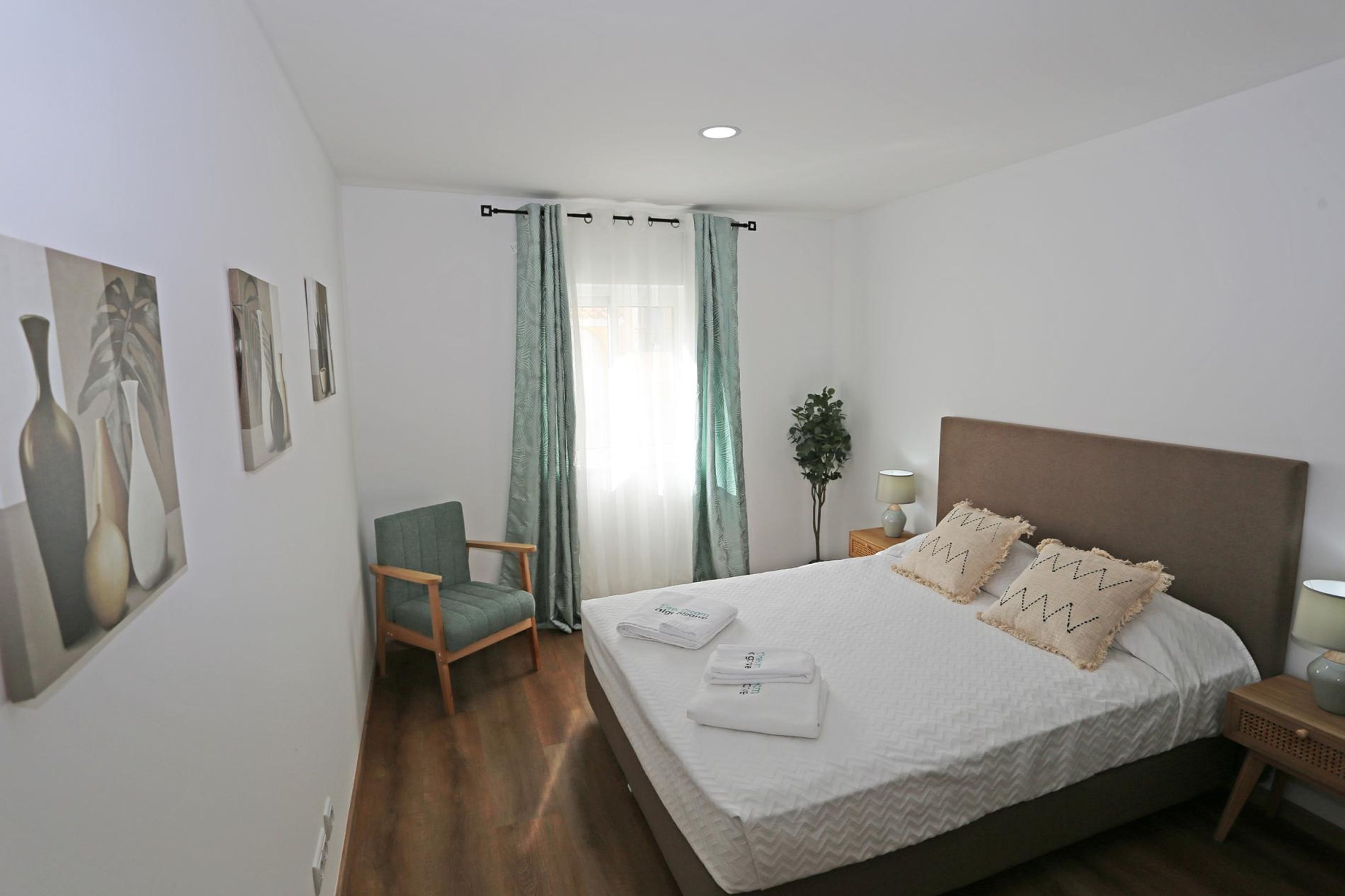 A neatly arranged hotel room with a large bed, a chair, a nightstand, and a potted plant.