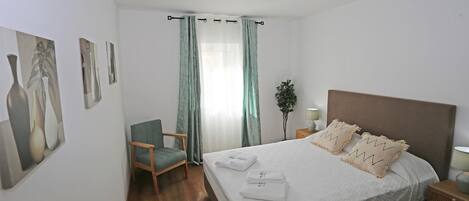 A neatly arranged hotel room with a large bed, a chair, a nightstand, and a potted plant.