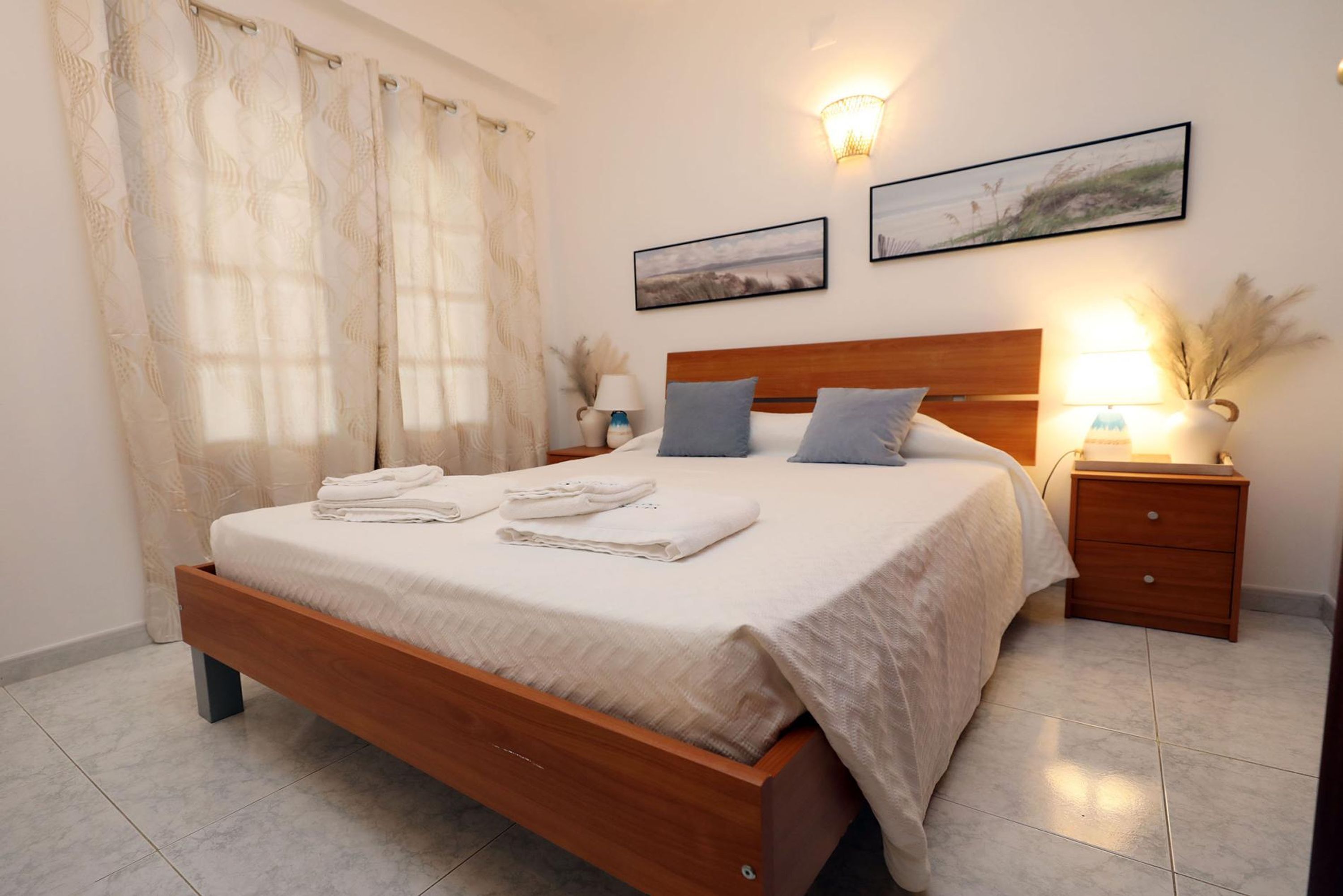 A neatly made bed with folded towels, a wooden headboard, and two bedside lamps.