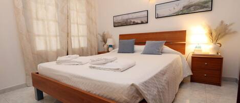 A neatly made bed with folded towels, a wooden headboard, and two bedside lamps.