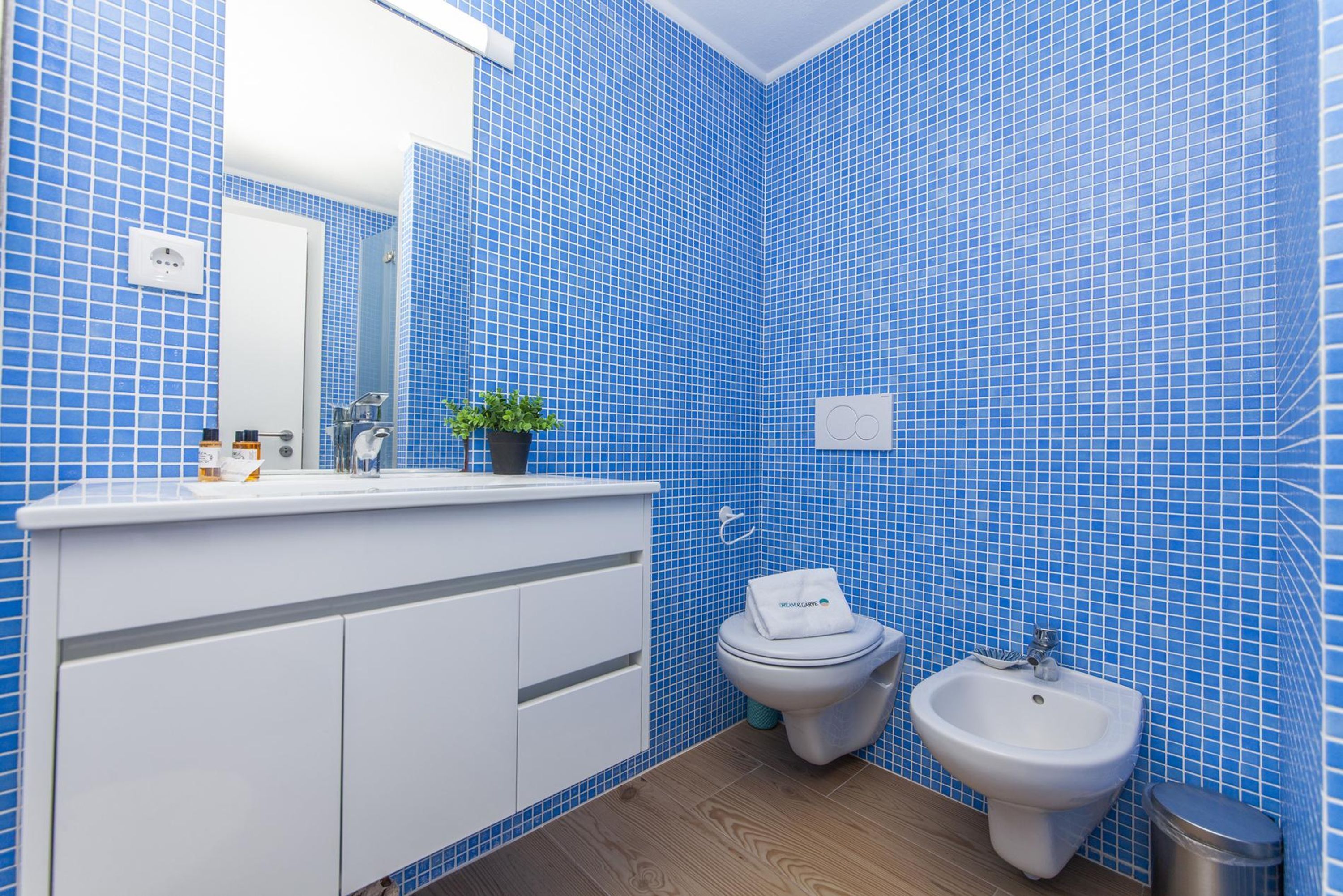 A bathroom with blue tiled walls, a white sink, a toilet, and a bidet.