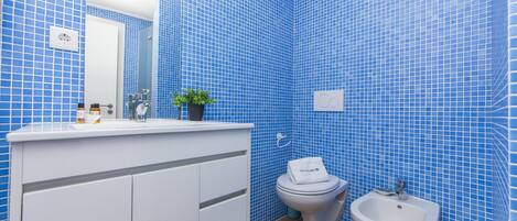 A bathroom with blue tiled walls, a white sink, a toilet, and a bidet.