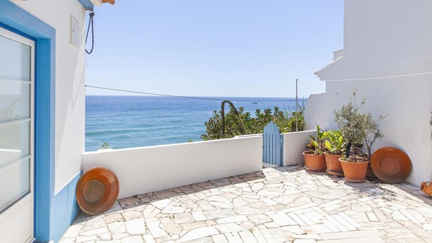Un balcon donnant sur la mer, agrémenté de plantes en pot et d’une porte bleue.