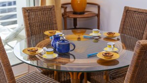 A round glass table with a tea set, plates, and cups, surrounded by wicker chairs in a room with a lamp and a window. - A69 - Felicidade Marina Apartment (Lagos)