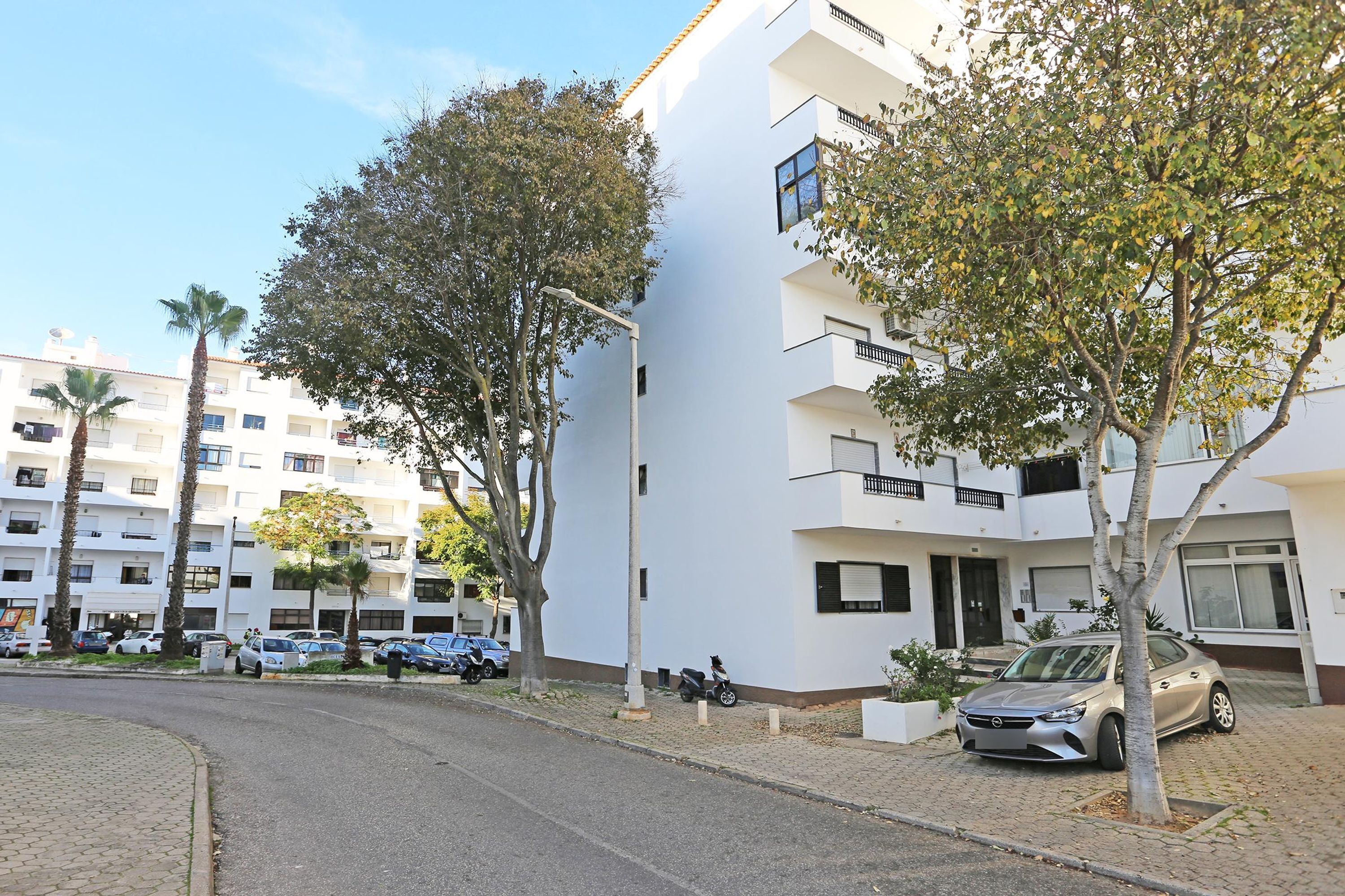 A modern apartment building with multiple balconies, a paved driveway, and parked cars.