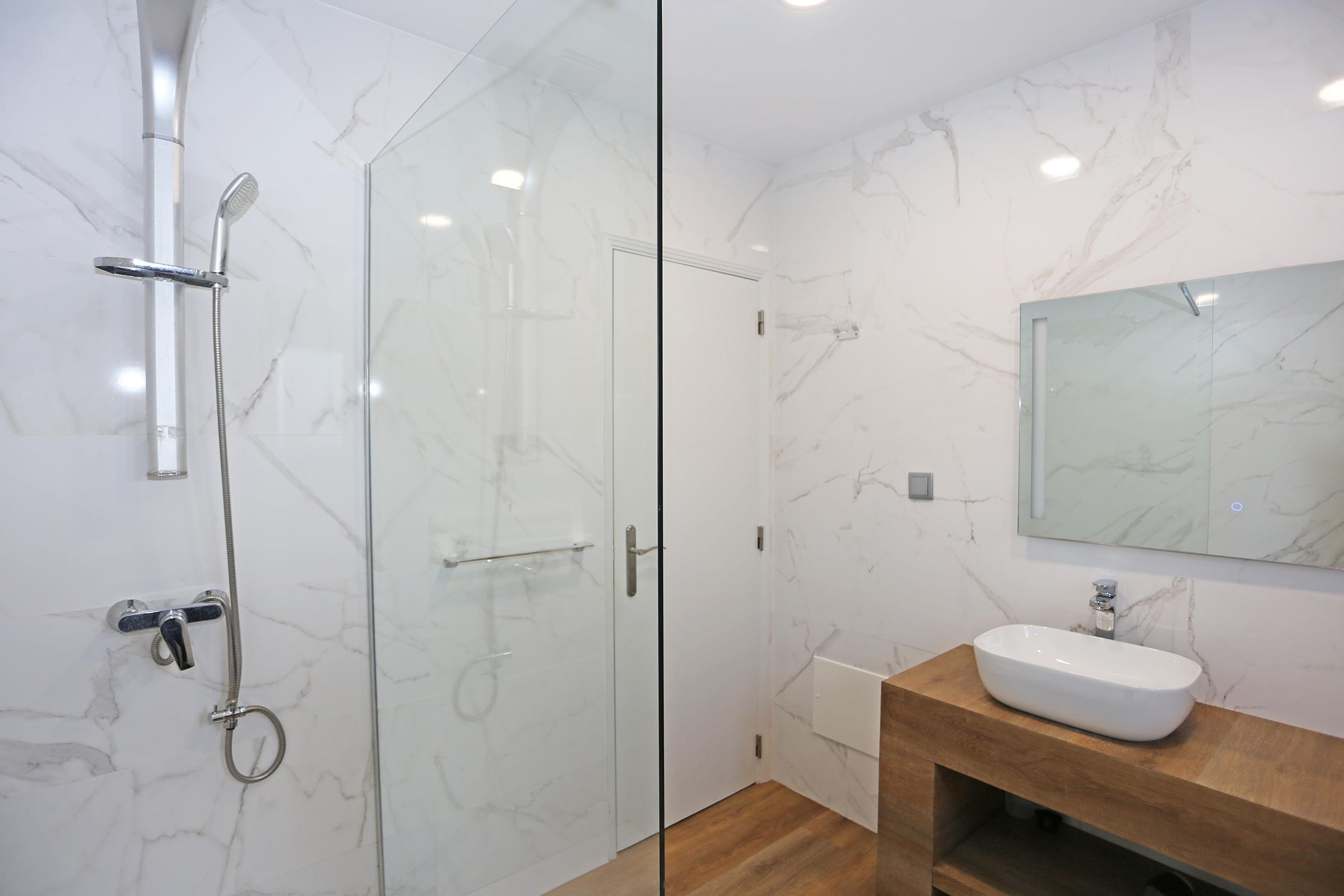 A modern bathroom with a glass shower enclosure, a wooden vanity with a white sink, and a marble-patterned wall.