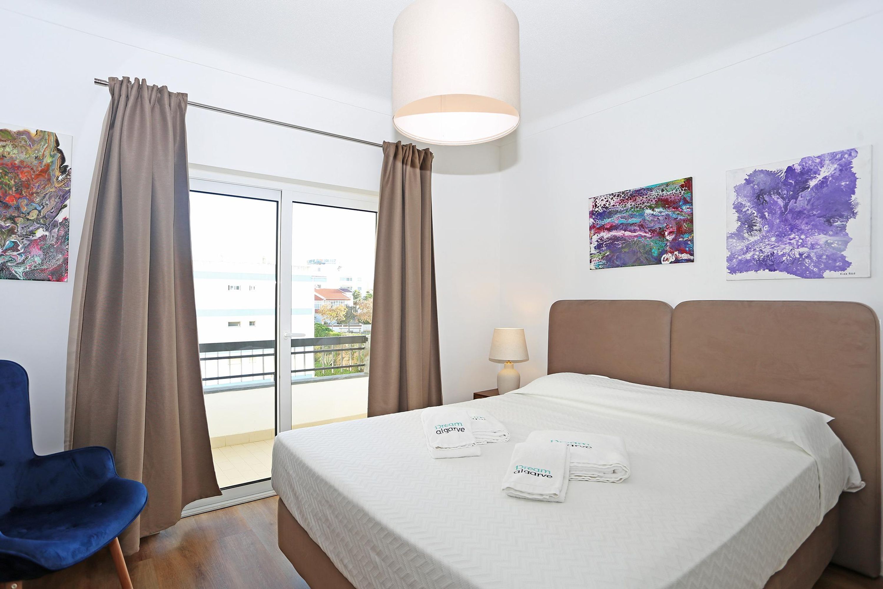 Une chambre d’hôtel avec un lit, une chaise, un balcon et des œuvres d’art accrochées aux murs.