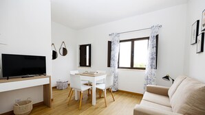 A modern living room with a flat-screen TV, a dining table with chairs, a sofa, and a window with curtains. - A48 - Windmill 1 Bed Apartment in Odiaxere (Lagos)