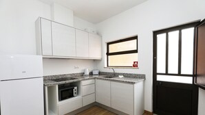 A compact kitchen with white cabinets, a granite countertop, a built-in oven, and a window with blinds. - A48 - Windmill 1 Bed Apartment in Odiaxere (Lagos)