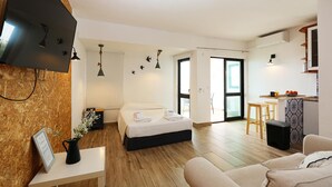 A modern hotel room with a bed, a small table with a vase, a sofa, a kitchen area, and a TV mounted on the wall. - A57 - Lighthouse Apartment in Via Dona Ana Lagos (Lagos)
