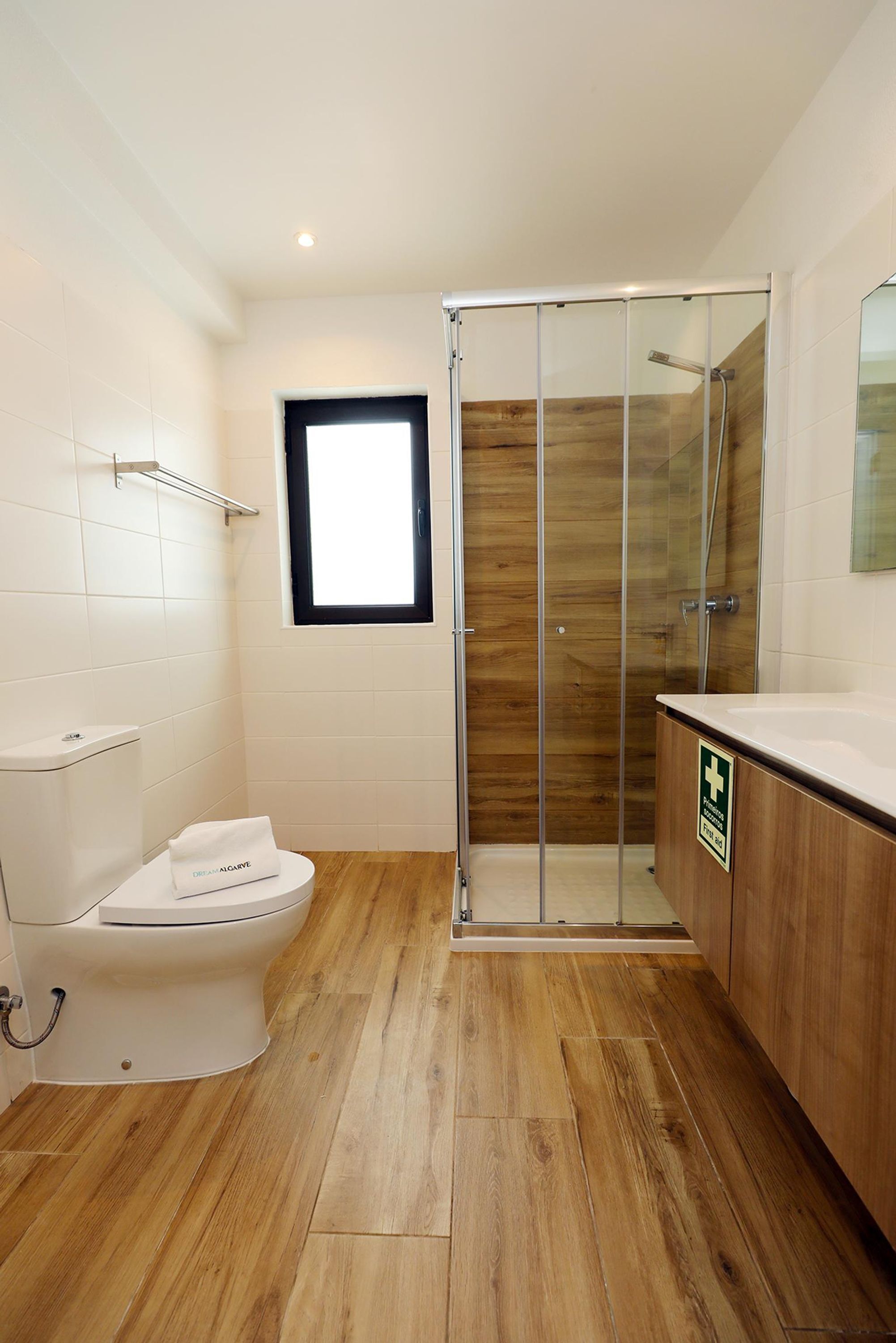 Un baño moderno con inodoro blanco, ducha con mampara de vidrio y piso de madera.