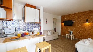 A compact kitchen with a dining area, a sofa, and a TV mounted on a wooden wall. - A57 - Lighthouse Apartment in Via Dona Ana Lagos (Lagos)
