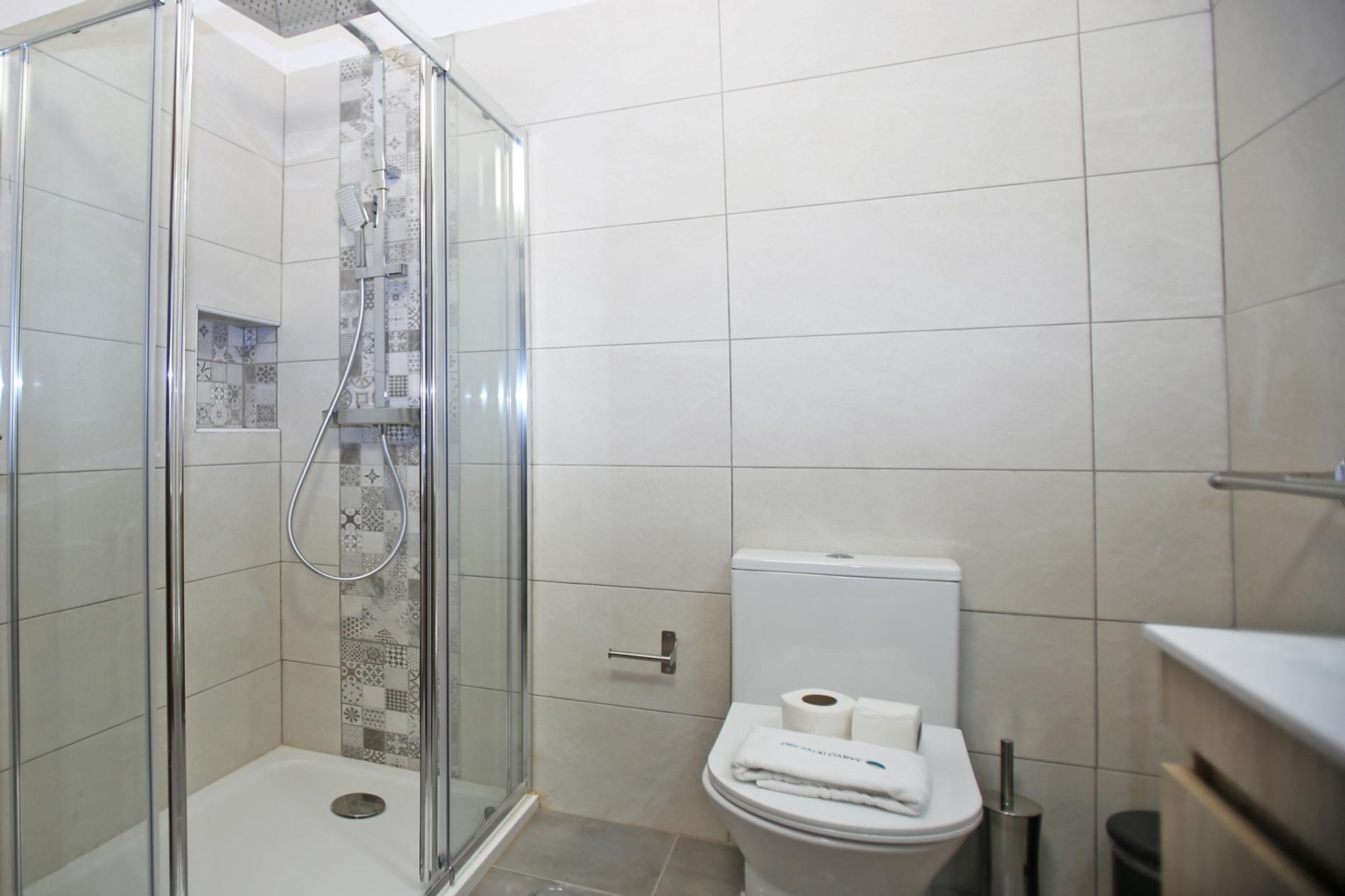 A modern bathroom with a glass-enclosed shower, a toilet with a white lid, and a patterned tile backsplash.