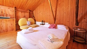 Une pièce chaleureuse aux murs en bois, avec un lit, un fauteuil jaune et une petite table sur laquelle est posée une lanterne.