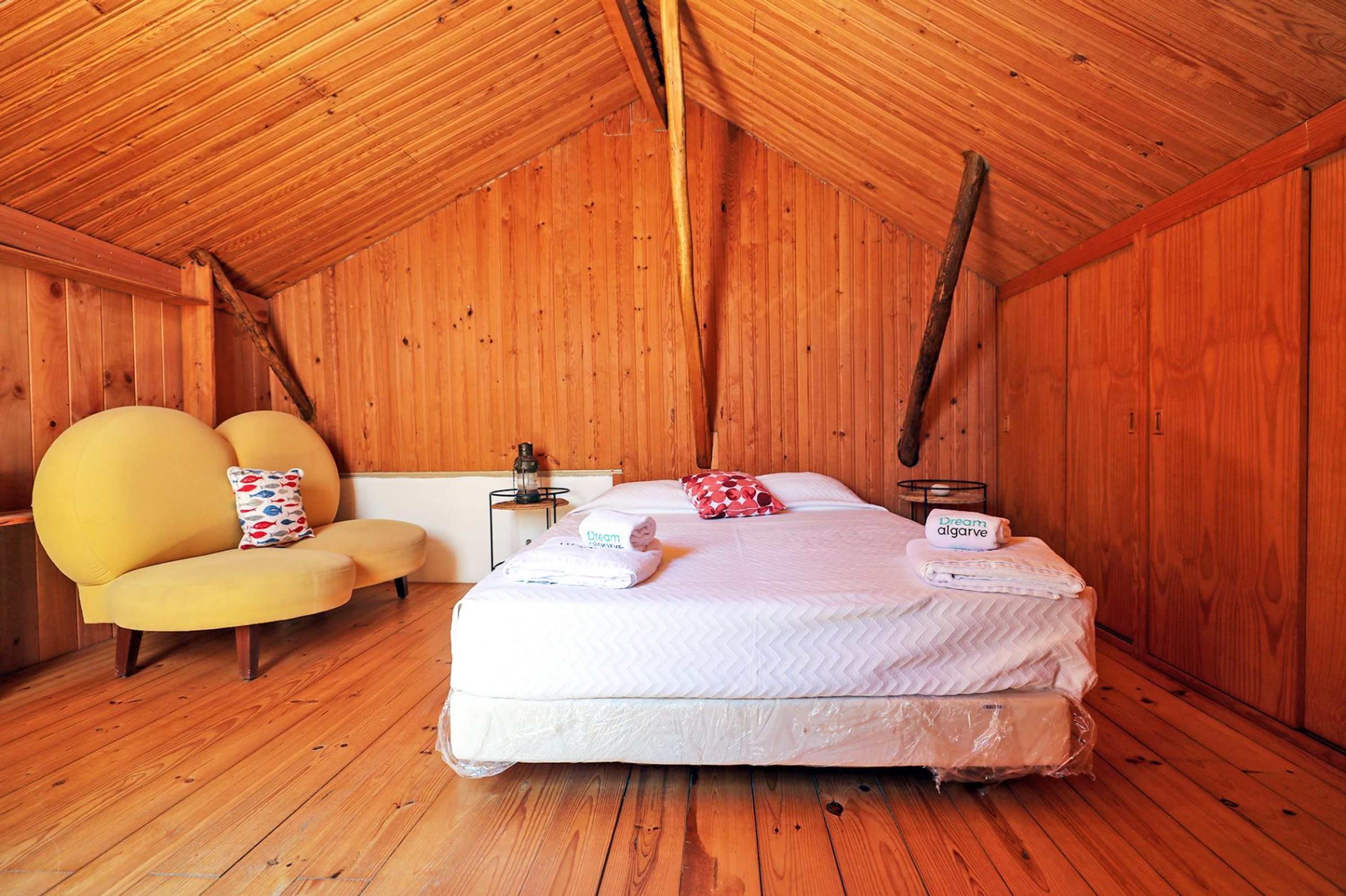 Um quarto acolhedor de madeira com uma cama, uma poltrona amarela e uma mesinha de cabeceira.